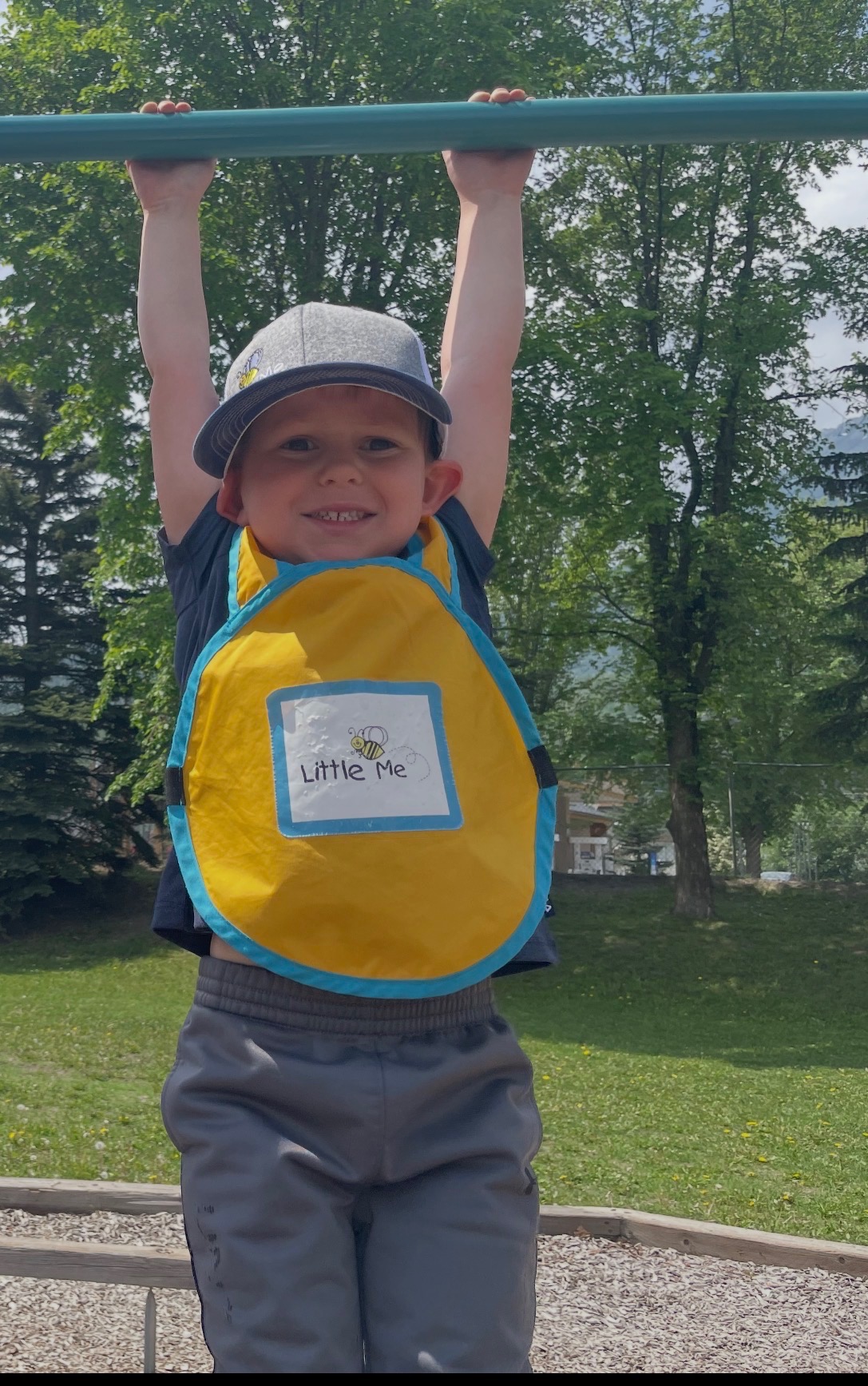 A smiling Little Me child in a yellow program apron enjoying active outdoor play